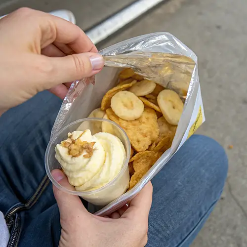 Hand holding a bag of chips filled with Walking Banana Pudding.
