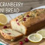 Freshly baked LEMON CRANBERRY ZUCCHINI BREAD with a slice cut out, displaying its moist texture and colorful ingredients.