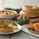 christmas brunch ideas table with smoked salmon bagels, spinach quiche, baked eggs, fruit salad and mini croissants