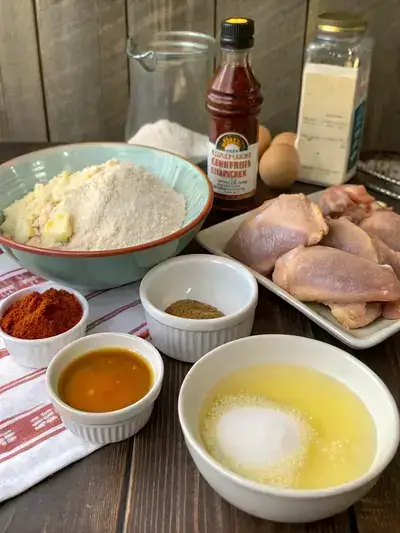 Ingredients for honey hot chicken displayed on a kitchen table, including chicken, buttermilk, eggs, flour, and spices.