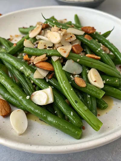Green beans tossed with toasted almonds, garlic, and seasoning on a white plate.