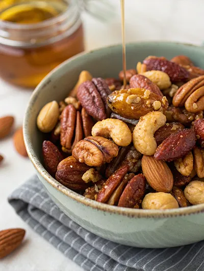Bowl of mixed nuts as honey drizzles over almonds, pecans, and cashews.