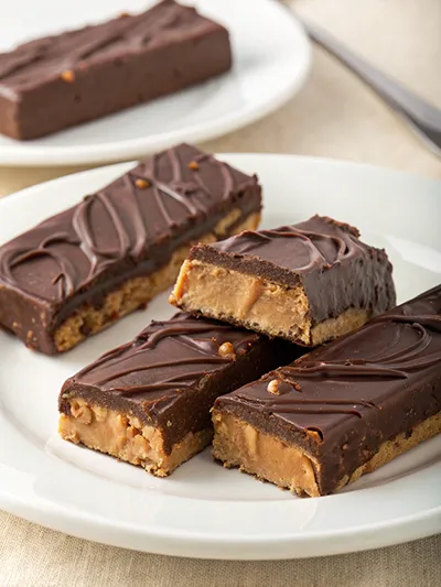 Chocolate-covered peanut butter bars with a cookie crust, sliced into squares on a white plate.