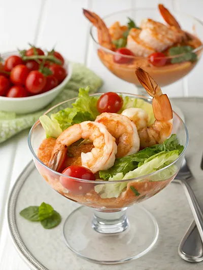 Prawn cocktail served in a glass with lettuce, cocktail sauce, and cherry tomatoes.