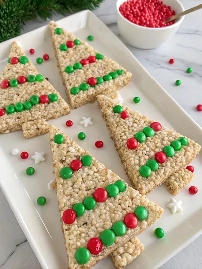 Rice Krispies treat Christmas trees decorated with red and green candies on a white tray.
