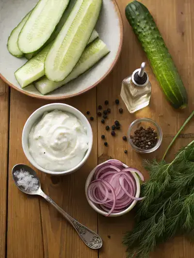 A variety of fresh ingredients for creamy cucumber salad displayed on a kitchen table.
