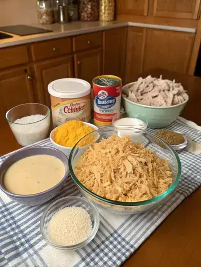 A variety of ingredients for Ritz Cracker Chicken Casserole displayed on a kitchen table, including chicken, crackers, soup, sour cream, milk, cheese, onion, butter, garlic powder, and seasonings.