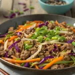 A delicious keto egg roll in a bowl with ground meat, cabbage, and carrots garnished with green onions and sesame seeds.